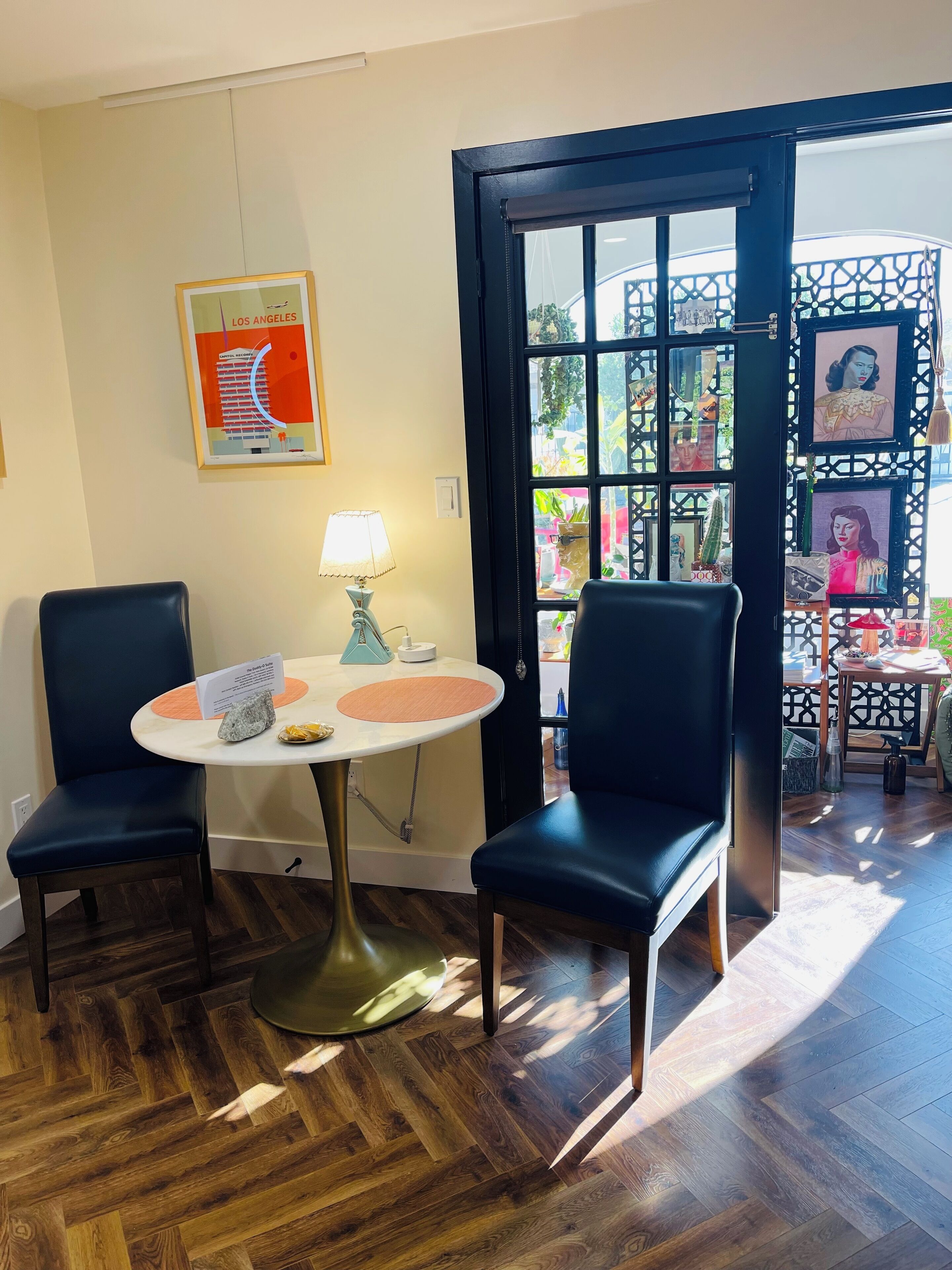 Une pièce avec deux fauteuils bleu foncé, une table ronde avec un plateau blanc, une lampe et un tableau encadré accroché au mur.