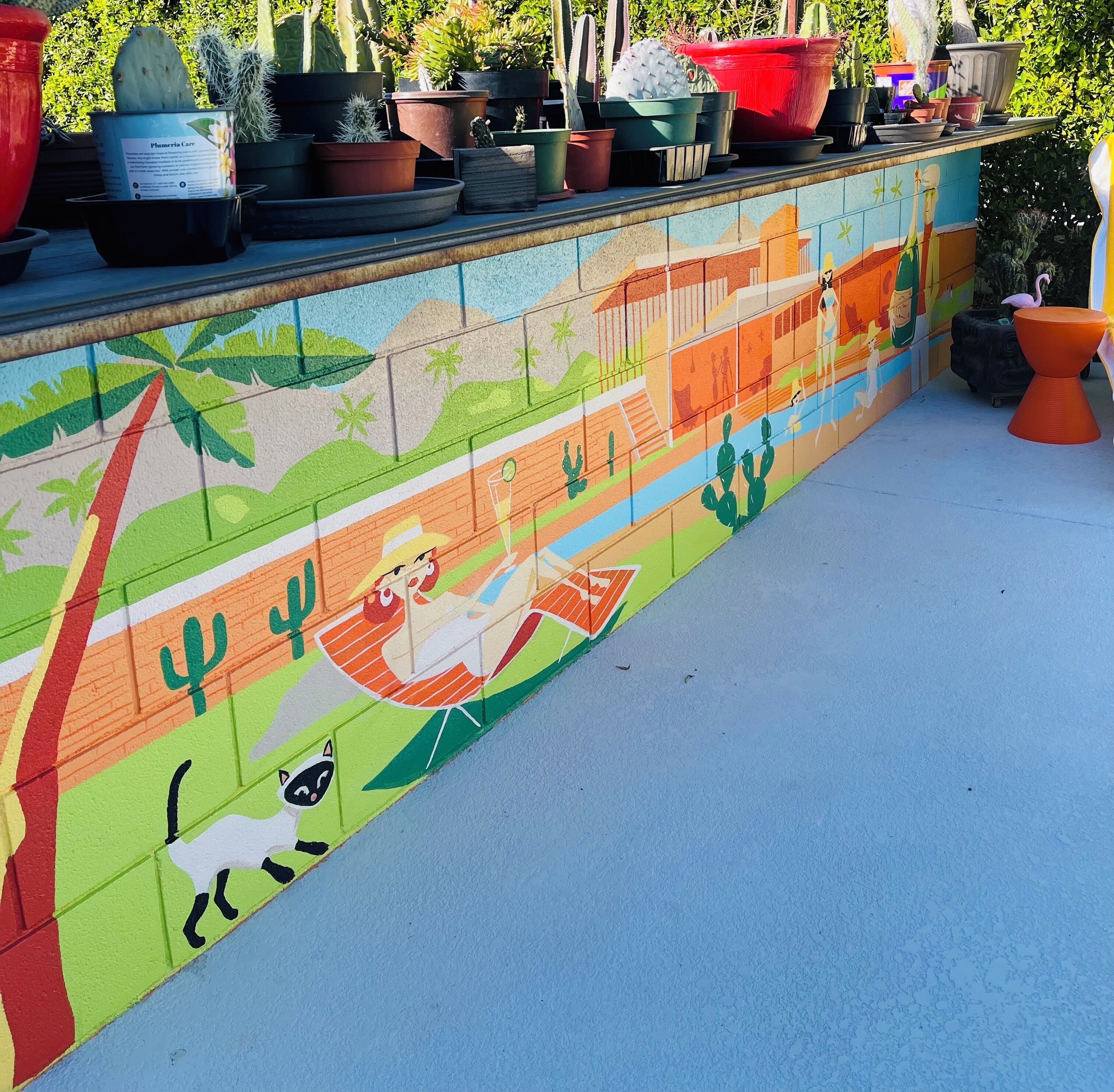 Un mural colorido con una mujer en una hamaca, cactus y un gato.