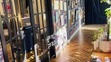 A room with a wooden herringbone floor, a black-framed door, and a wall with framed pictures and a sign that reads "LIVE BY THE SUN LOVE BY THE MOON".