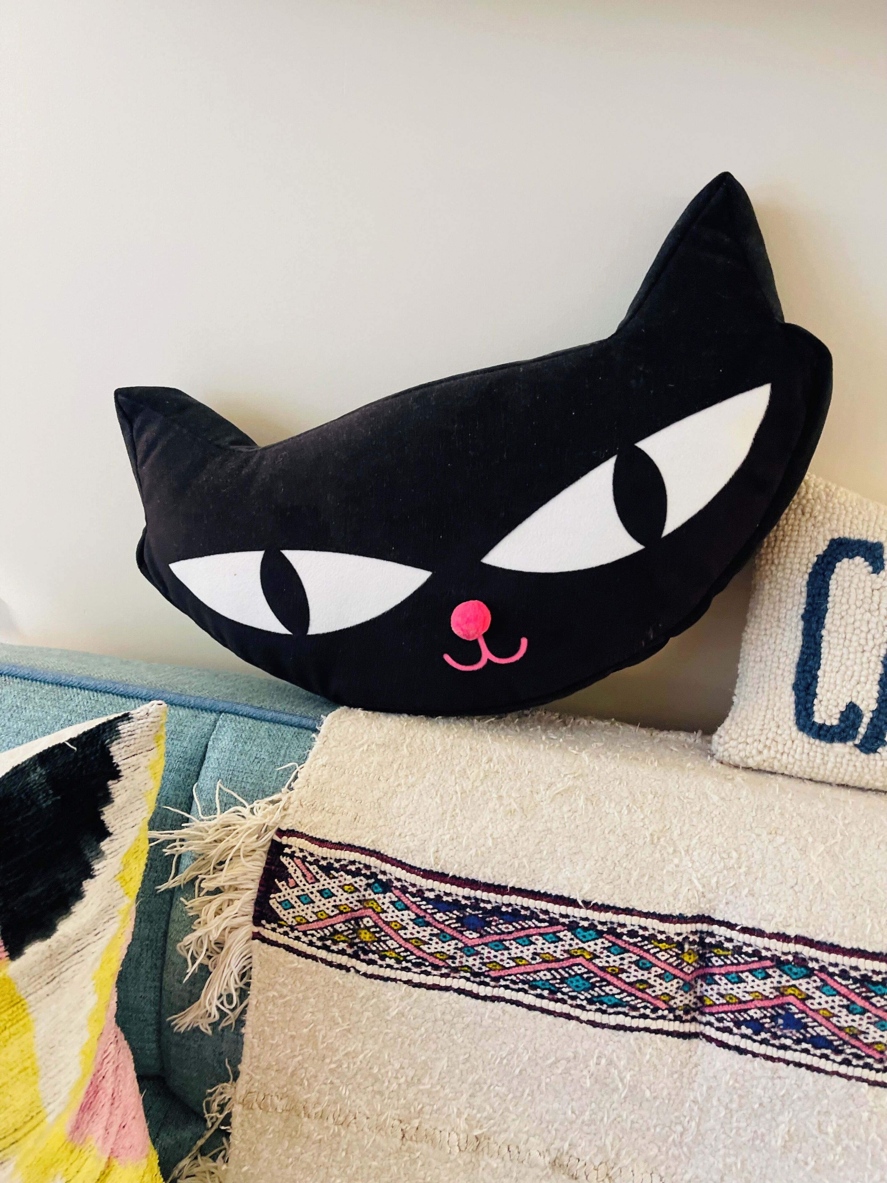 A black cat-shaped pillow with a pink nose on a couch.