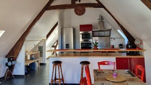 Une cuisine avec un plafond orné de poutres en bois, un îlot central doté de tabourets et des meubles de rangement rouges.