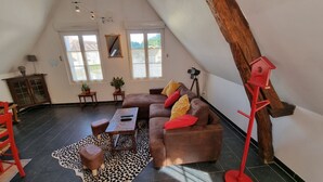 Un loft spacieux avec un plafond haut, un grand canapé en cuir marron, une table basse en bois et un lampadaire rouge.