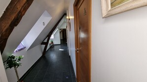 Un couloir étroit avec un plafond en pente, une porte en bois et un tableau encadré accroché au mur.