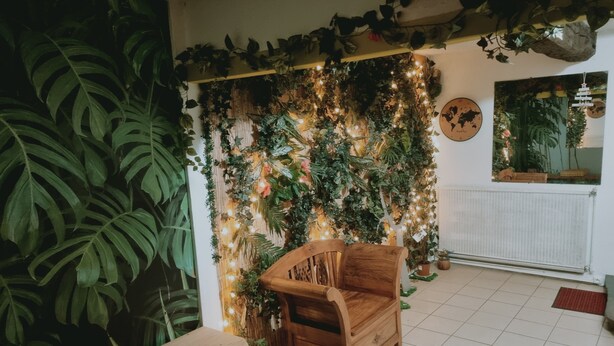 Une pièce chaleureuse avec une chaise en bois, une petite table et un mur décoré de plantes et de guirlandes lumineuses.