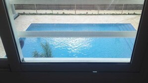 Vista de una piscina a través de una ventana, con una zona de arena visible en el exterior.