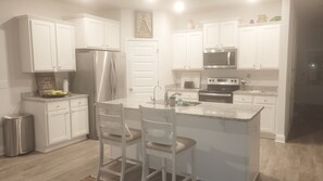 A modern kitchen with white cabinetry, stainless steel appliances, and a central island with bar stools.
