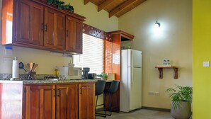 A kitchen with wooden cabinets, a refrigerator, a countertop with kitchen appliances, and a potted plant. - Eden Villas (Corinth)