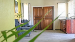 A room with a wooden door, a sofa, a small table with a plant, and a kitchen area with cabinets and a sink. - Eden Villas (Corinth)
