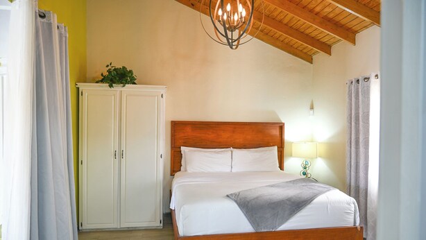 A bedroom with a wooden bed, a white wardrobe, a chandelier, and a lamp. - Eden Villas (Corinth)