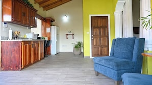 A kitchen with wooden cabinets, a refrigerator, and a dining area with a blue sofa. - Eden Villas (Corinth)
