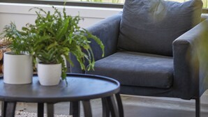 Uma sala de estar moderna com um sofá cinzento, uma mesa redonda preta e dois vasos brancos com plantas verdes.