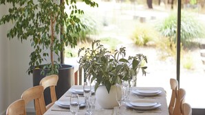 Mesa de jantar posta para quatro com vista para um jardim através de grandes janelas.