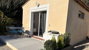 Ein kleines Gebäude mit Terrasse, einer Schiebetür und einem Grill.