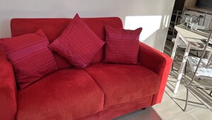 Ein rotes Sofa mit gemusterten Kissen in einem modernen Wohnbereich mit Esstisch und Stühlen.