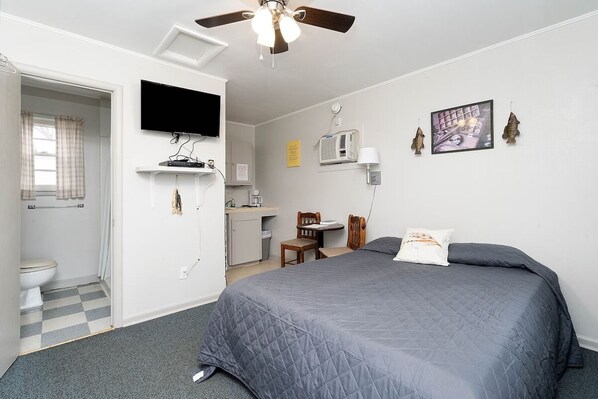 A bedroom with a bed, a desk, a chair, a television, and a ceiling fan.