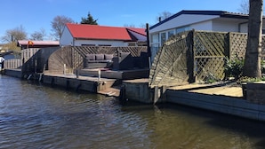 Une propriété située au bord de la rivière, dotée d’un quai en bois, d’un espace de détente avec un canapé et une table, et d’une maison avec un toit rouge.