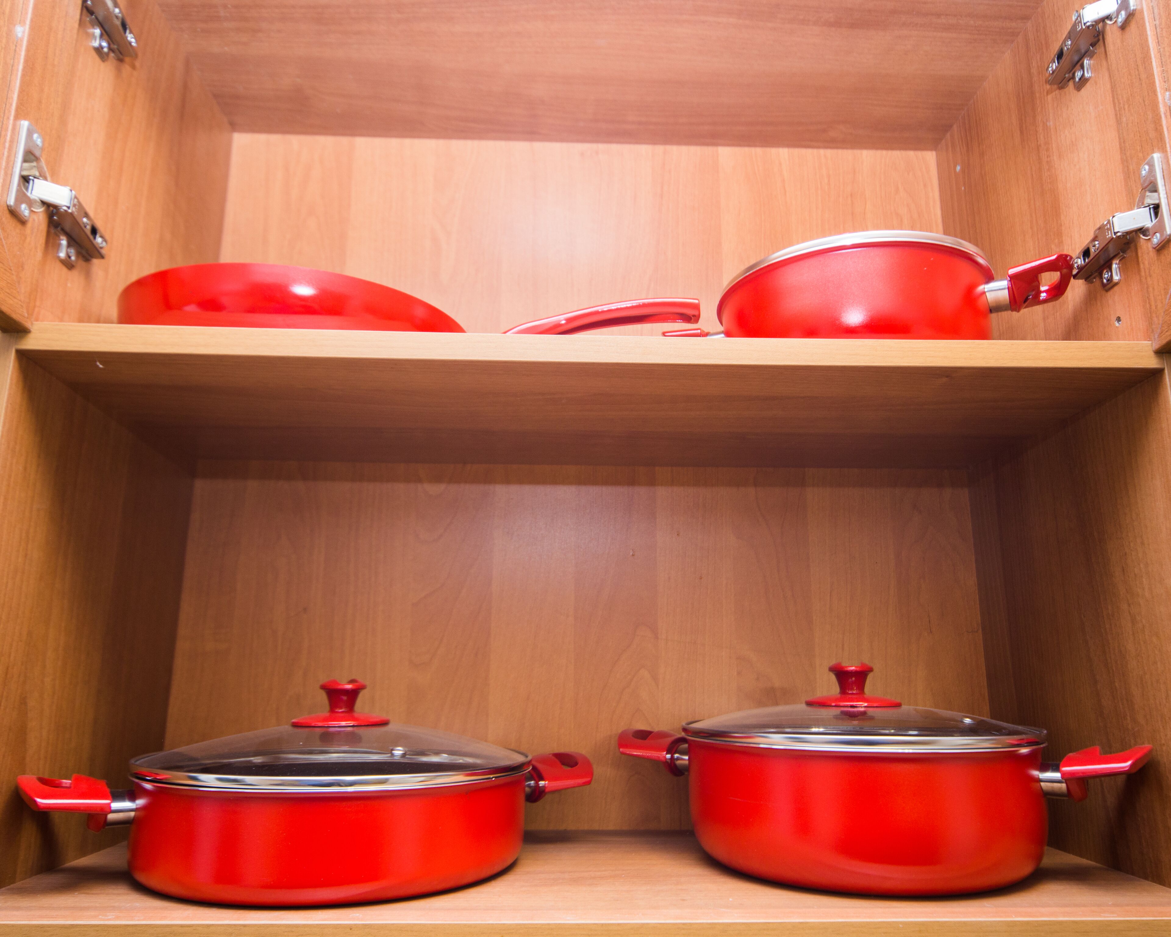 Un meuble de cuisine contenant deux casseroles rouges et une poêle rouge.