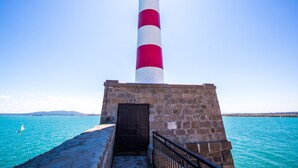 Um farol com torre listrada em vermelho e branco, base de pedra e uma porta.
