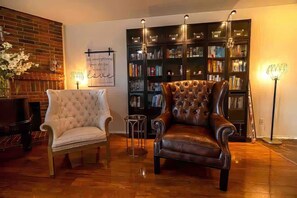 A cozy living room with a fireplace, a bookshelf, and two leather armchairs. - Hill Country Beauty in Red | Beautiful Large Home! Very Spacious! (Cedar Park)