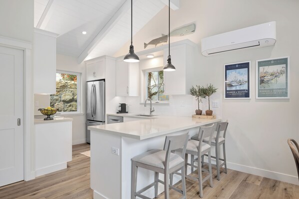 A modern kitchen with white cabinetry, a central island with bar stools, pendant lighting, and a large fish decoration on the wall.