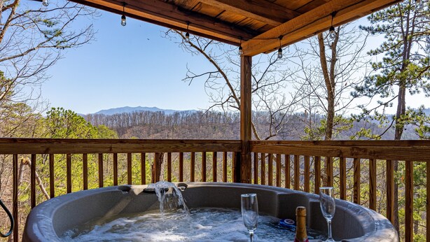 Een hottub met een glas en fles, omringd door een houten terras en met uitzicht op een bergachtig landschap.