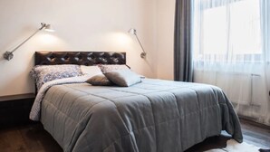 A neatly made bed with a grey duvet, two bedside lamps, and a window with sheer curtains. - Apartment (Minsk)