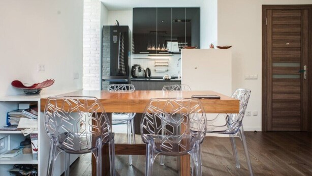 A modern kitchen with a wooden table and clear chairs, a white brick wall, and a wooden door. - Apartment (Minsk)