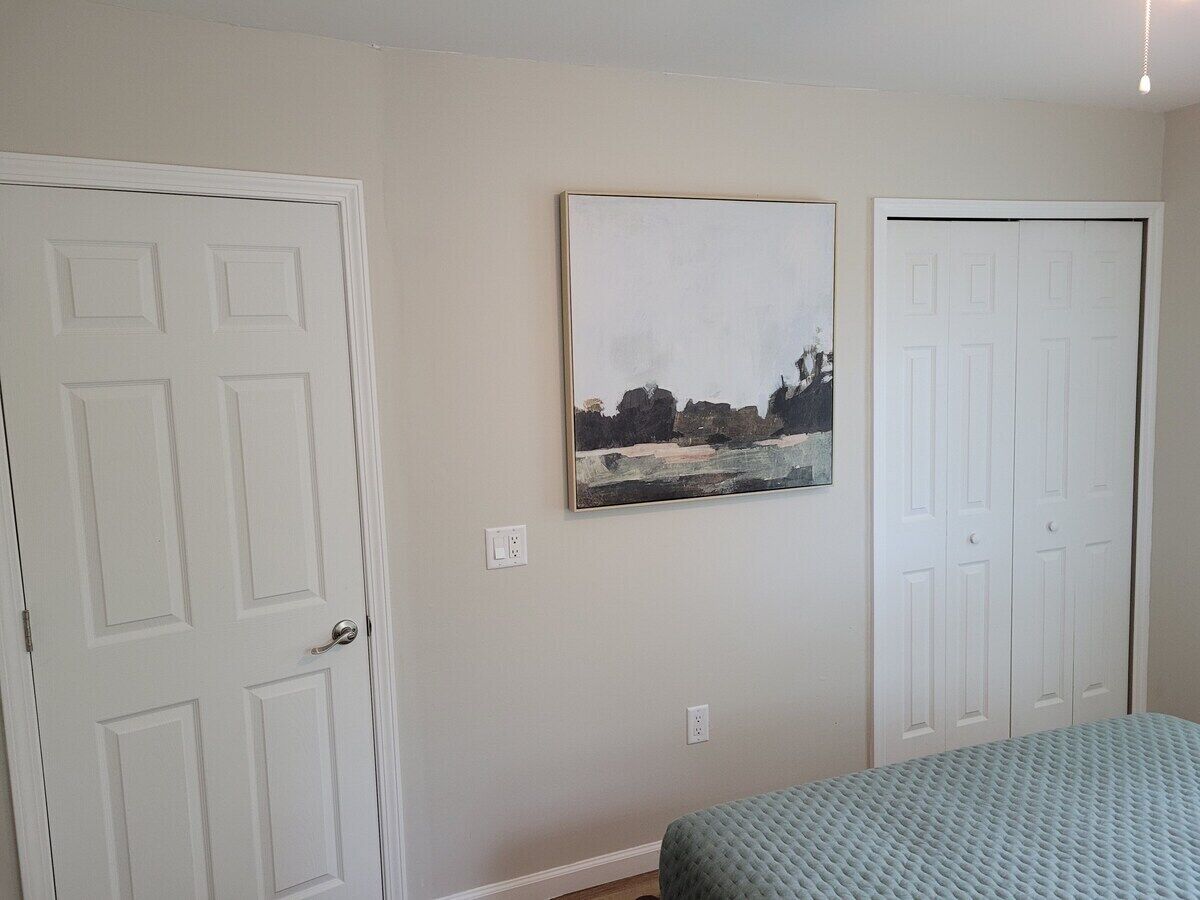 A bedroom with a bed, a door, and a painting on the wall.