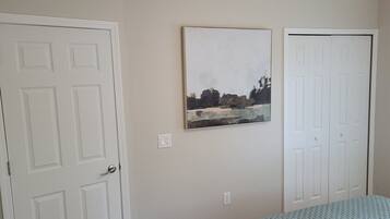 A bedroom with a bed, a door, and a painting on the wall.