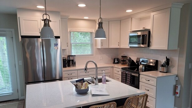 A modern kitchen with a central island, stainless steel appliances, and wicker chairs. - White Birch - Riverfront and Newly-Remodeled!  Great Location! (Elberta)