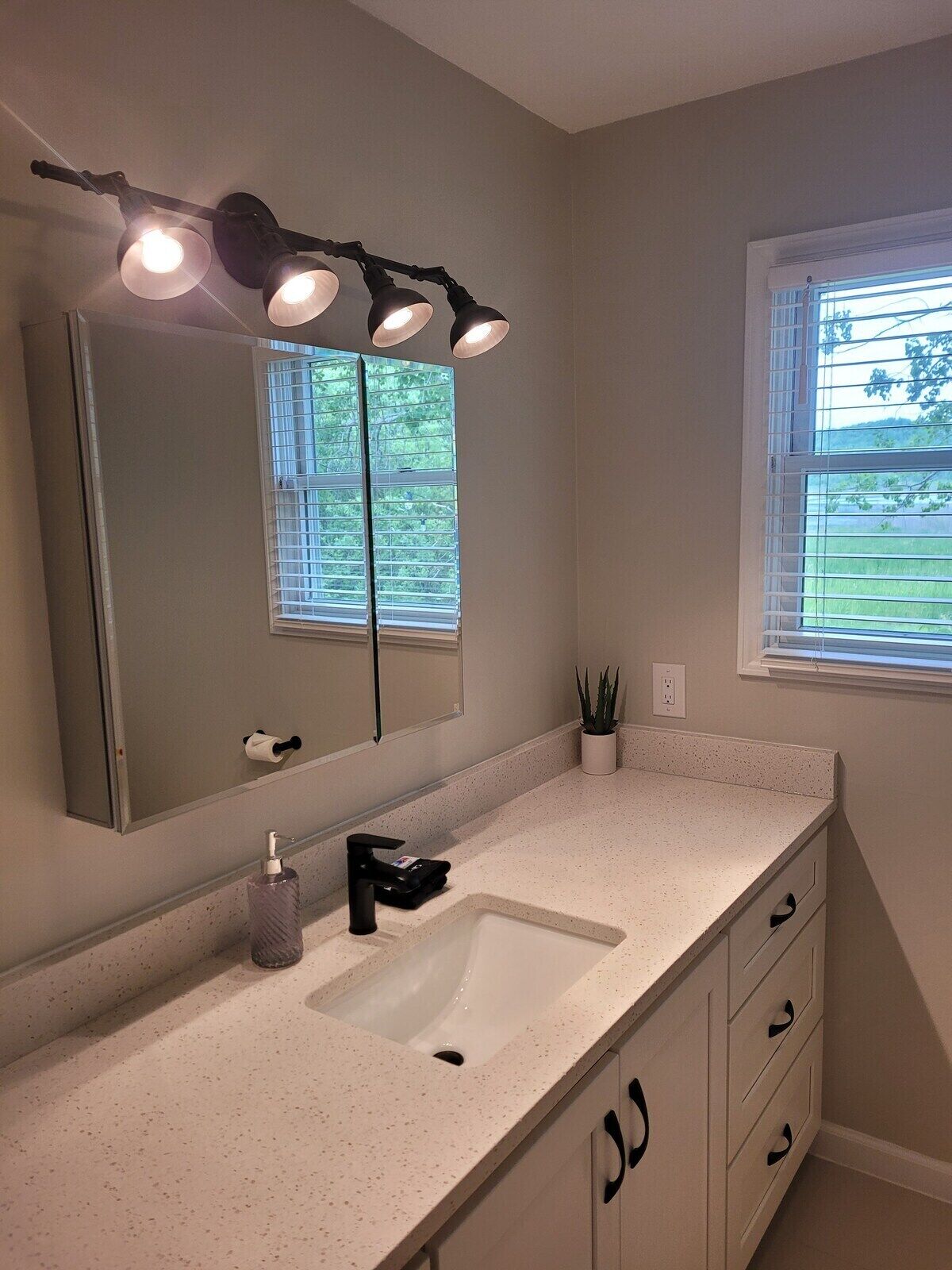 Une salle de bain avec un lavabo blanc, un grand miroir et un luminaire fixé au plafond.