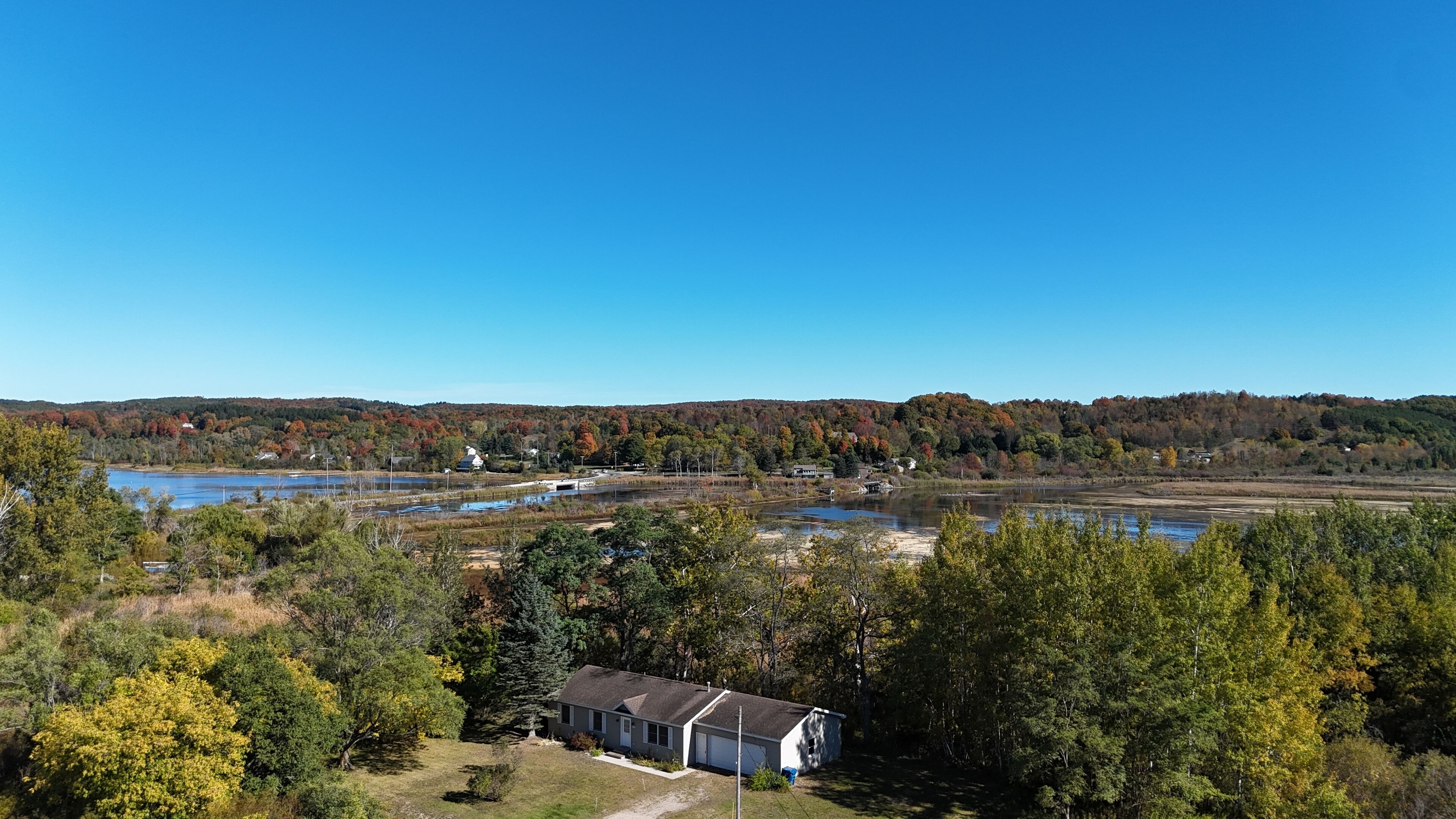 A lakeside property with a large house, a dock, and a forested backdrop.