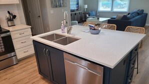 A modern kitchen with a stainless steel dishwasher, a double sink, and a white speckled countertop. - White Birch - Riverfront and Newly-Remodeled!  Great Location! (Elberta)