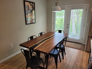 A dining area with a wooden table and chairs, a pendant light, a door with blinds, and a framed picture on the wall.