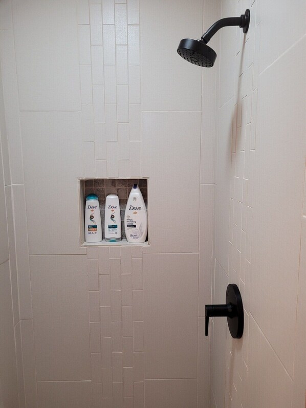 A shower with a black handheld showerhead, a tiled wall, and a shelf with Dove body wash bottles.
