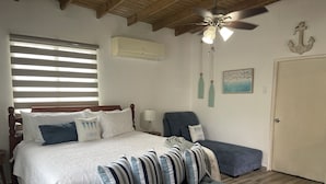 A bedroom with a bed, a bench, a ceiling fan, an air conditioner, and nautical-themed decor.