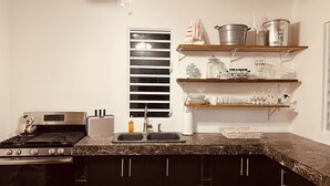 A kitchen with a stove, oven, and a sink. There are shelves with dishes and a ceiling fan.
