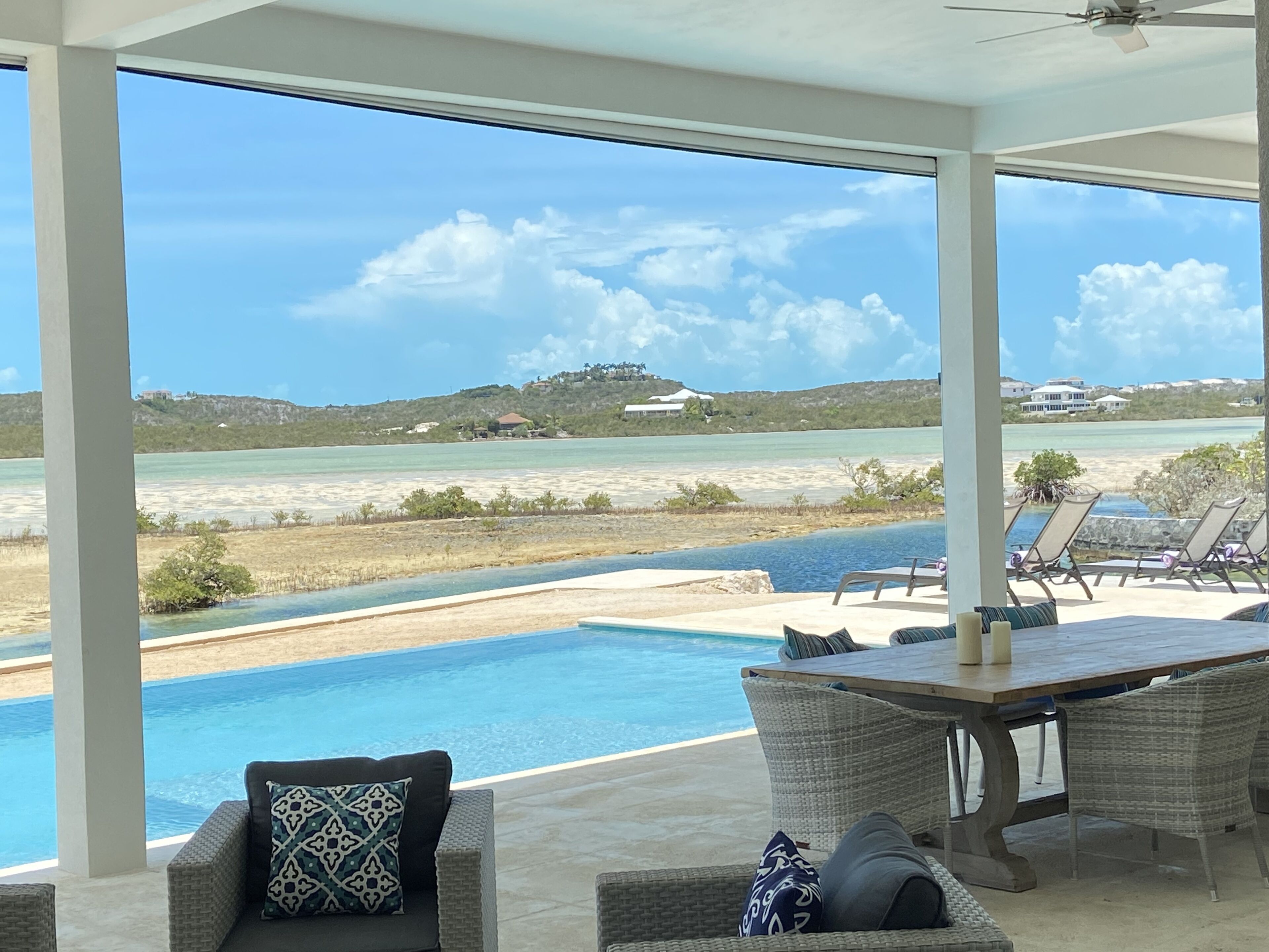 A poolside area with wicker furniture and a view of the ocean and hills.