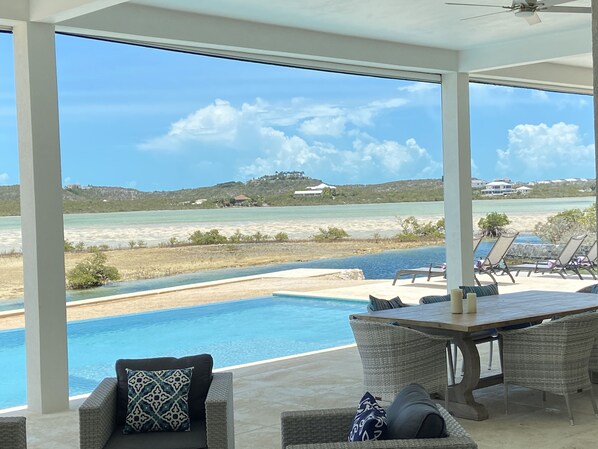 A poolside area with wicker furniture and a view of the ocean and hills.