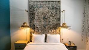 A neatly made bed with white linens, two bedside lamps, a small bedside table, and a wall tapestry. - Numero Uno Piñones Short Term Rental (Loiza)