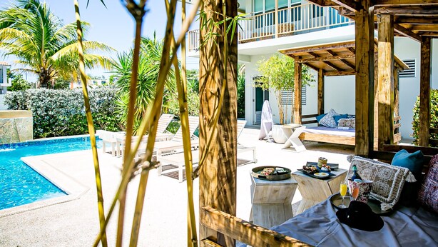 A poolside area with a wooden pergola, lounge chairs, and a dining table with food and drinks. - Numero Uno Piñones Short Term Rental (Loiza)