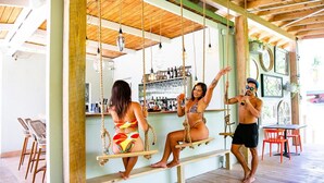 A bar area with wooden beams, a swing set, and a bar counter with bottles. - Numero Uno Piñones Short Term Rental (Loiza)