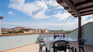 Una terrazza con un tavolo apparecchiato per mangiare, affacciata su una zona residenziale con case e cielo sereno.