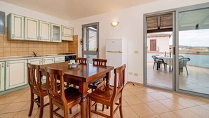 Una cucina con tavolo e sedie, un frigorifero e una porta vetrata scorrevole che dà su un patio esterno.