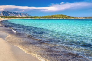 Una playa con aguas turquesas cristalinas, una orilla arenosa y montañas al fondo.