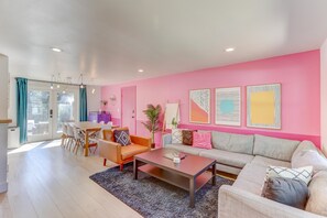 Ein modernes Wohnzimmer mit einer rosafarbenen Wand, einem grauen Sofa, einem Holzesstisch und einem Couchtisch.