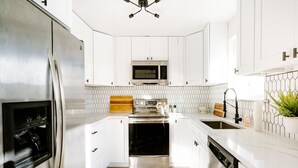A modern kitchen with white cabinetry, stainless steel appliances, and a wooden cutting board. - Spacious 5-Bedroom Retreat - Hot Tub - Games (Denver)