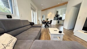 Una sala moderna con un sofá gris, una mesa de centro blanca y un área de comedor al fondo.