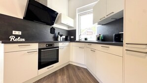 Una cocina moderna con horno empotrado, microondas y televisor negro montado en la pared.