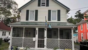 Une maison à deux étages avec un porche à l’avant, un drapeau et une pancarte indiquant « À louer ».